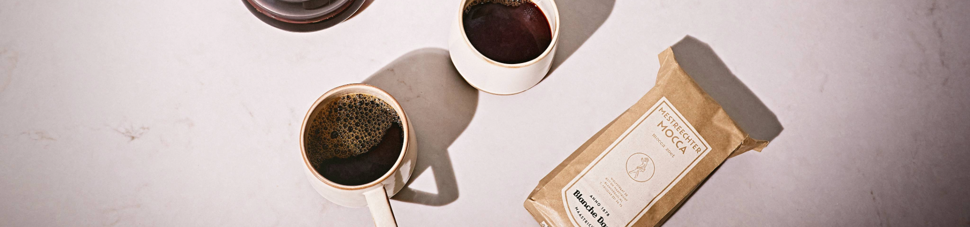 Hero-afbeelding met twee kopjes versgezette koffie en een zak Blanche Dael Mestreechter Mocca op een lichte ondergrond